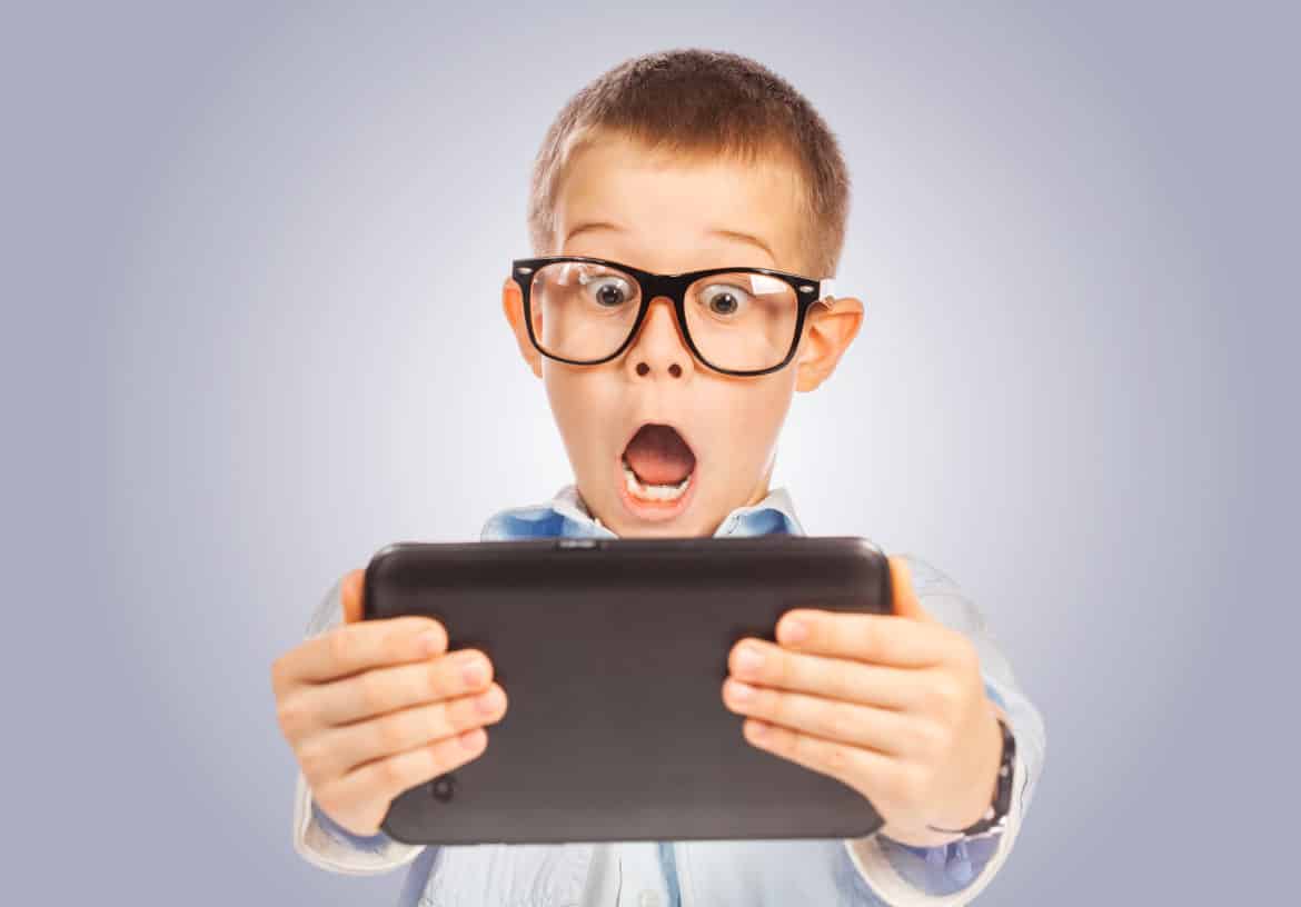 Surprised boy with tablet against a grey background 
** Note: Shallow depth of field