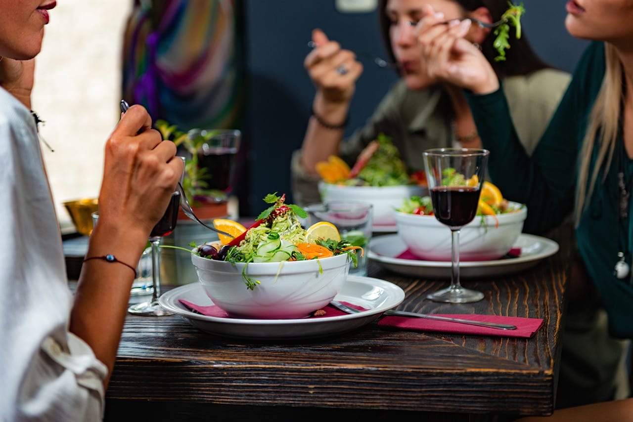 Vegetarian Restaurant. Cheerful Female Friends Enjoying Fresh Salad in Restaurant and Having Fun.