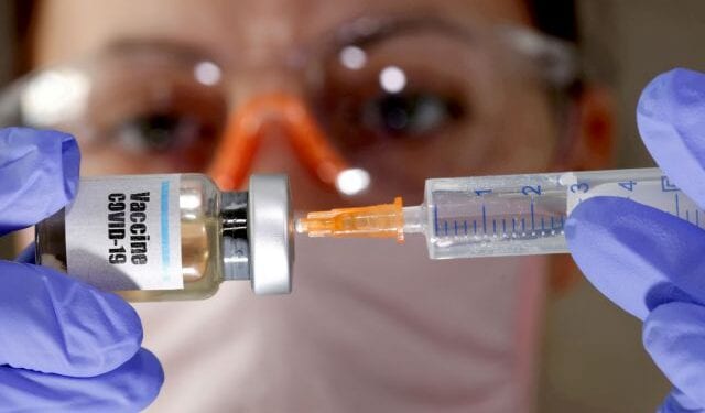 FILE PHOTO: A woman holds a small bottle labeled with a "Vaccine COVID-19" sticker and a medical syringe in this illustration taken April 10, 2020. REUTERS/Dado Ruvic//File Photo