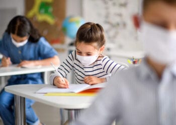 Small children with face mask back at school after covid-19 quarantine and lockdown, writing.