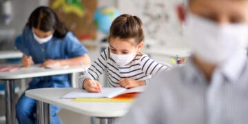 Small children with face mask back at school after covid-19 quarantine and lockdown, writing.