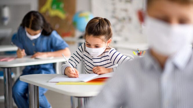 Small children with face mask back at school after covid-19 quarantine and lockdown, writing.