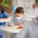 Small children with face mask back at school after covid-19 quarantine and lockdown, writing.