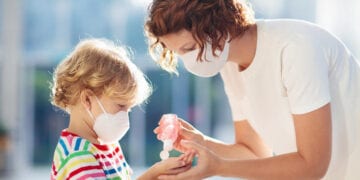 Family with kids in face mask in shopping mall or airport. Mother and child wear facemask during coronavirus and flu outbreak. Virus and illness protection, hand sanitizer in public crowded place.